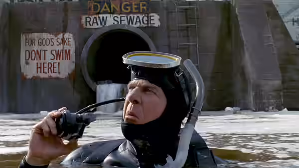Frank Drebin (Leslie Nielsen), wearing scuba gear, floats before a raw sewage outfall