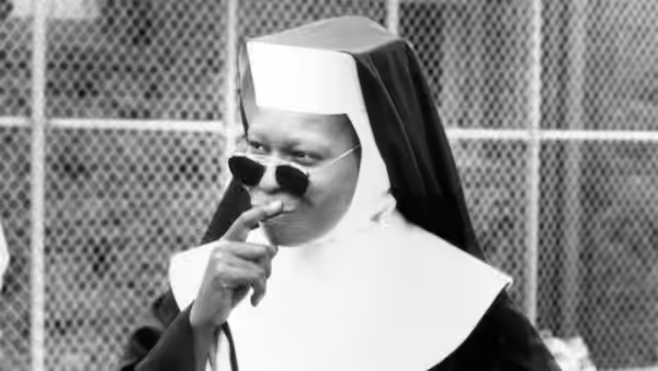 Deloris Van Cartier (Whoopi Goldberg) wears sunglasses and a nun's habit outside a chain-link fence