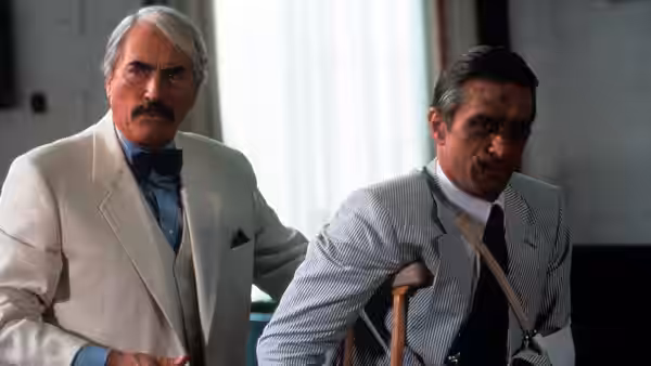 Lieutenant Elgart (Robert Mitchum) stands beside injured Sam Bowden (Nick Nolte), who leans on crutches