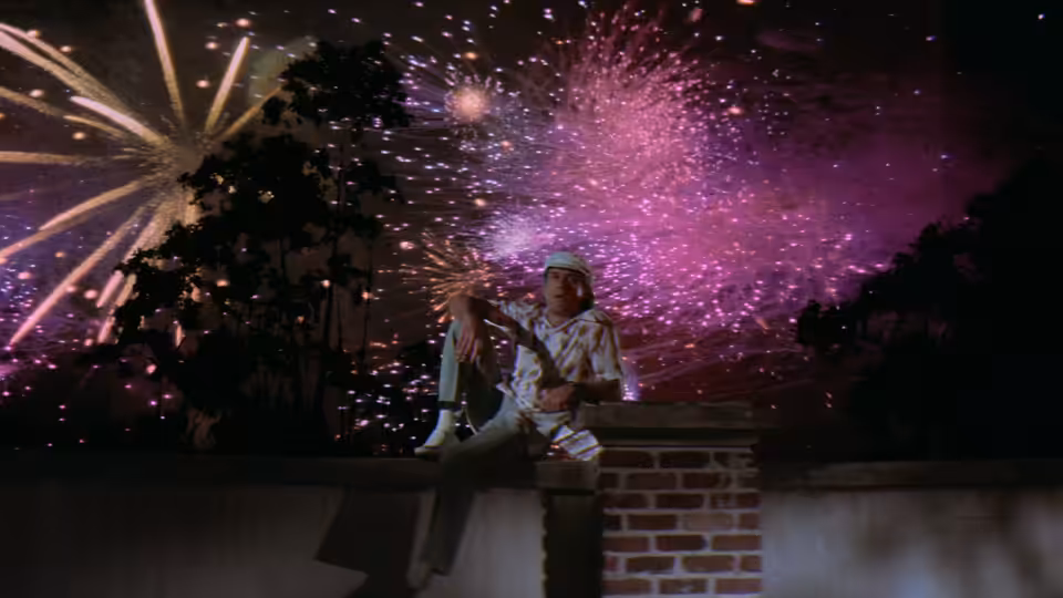 A woman sits on a brick wall as fireworks burst overhead