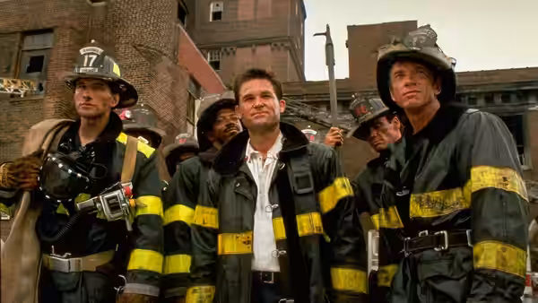 Firefighters stand together on a city street outside brick buildings
