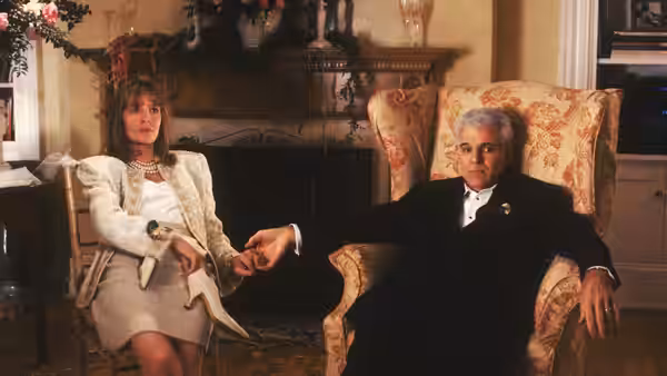 George and Nina Banks sit together in formal clothes beside a fireplace