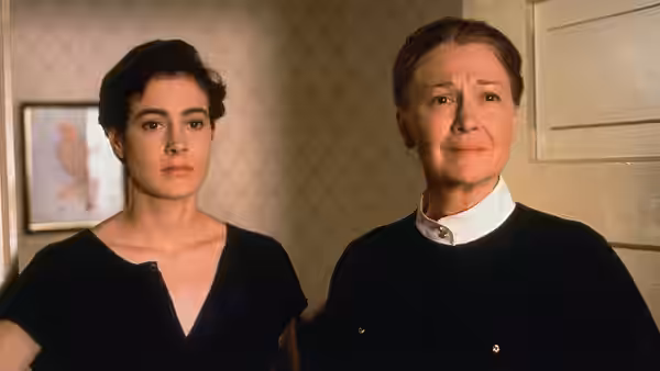 A young woman and an older woman stand together indoors, looking ahead