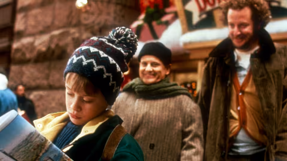 Kevin (Macaulay Culkin) reads a map while Harry and Marv approach on a city street