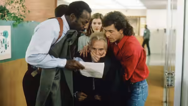 Roger Murtaugh (Danny Glover) and Martin Riggs (Mel Gibson) crowd around a paper with Leo Getz