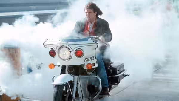 Martin Riggs (Mel Gibson) rides a police motorcycle through billowing smoke