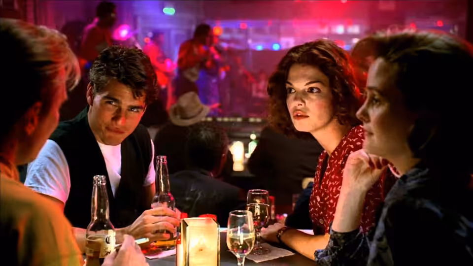 Mitch McDeere (Tom Cruise) sits at a nightclub table with Abby and another woman