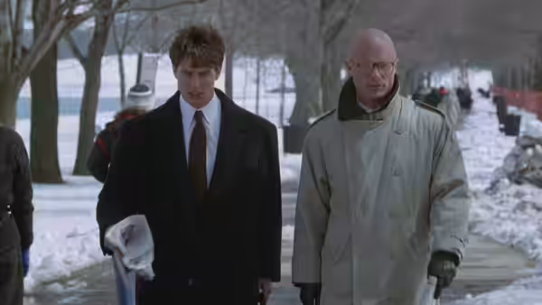 Mitch McDeere (Tom Cruise) walks through a snowy park beside a bald man in a coat