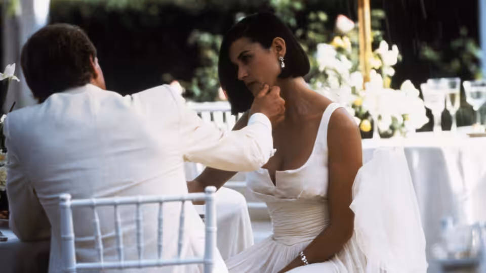 John Gage (Robert Redford) reaches toward Diana Murphy (Demi Moore) at an outdoor table