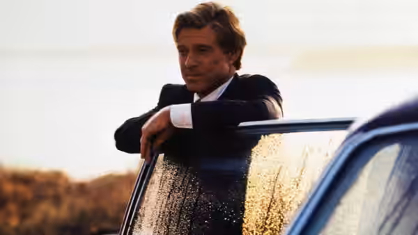 John Gage leans on a car door in a sunlit field