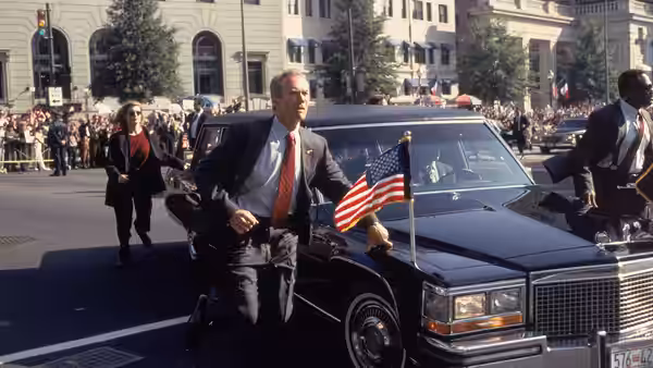 Frank Horrigan (Clint Eastwood) hurries beside a presidential limousine as agents escort it through a crowd
