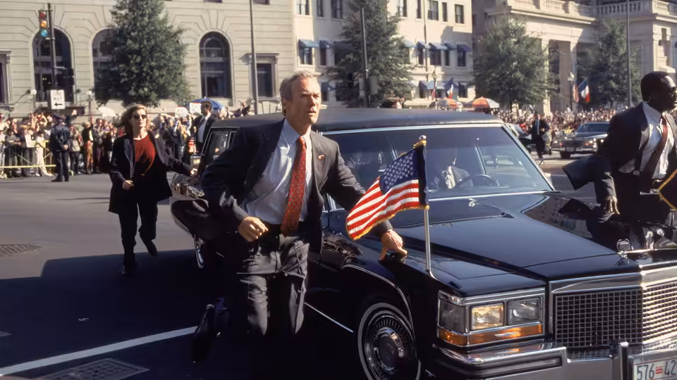 Frank Horrigan (Clint Eastwood) hurries beside a presidential limousine as agents escort it through a crowd