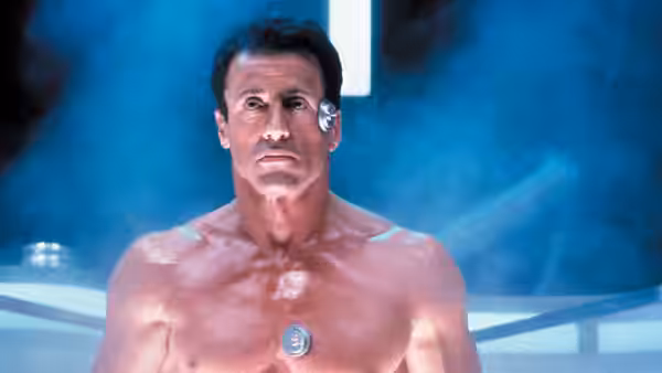 John Spartan (Sylvester Stallone) stands shirtless in a bright, blue-lit chamber
