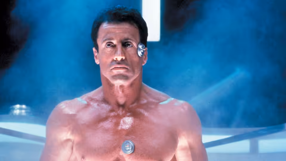John Spartan (Sylvester Stallone) stands shirtless in a bright, blue-lit chamber