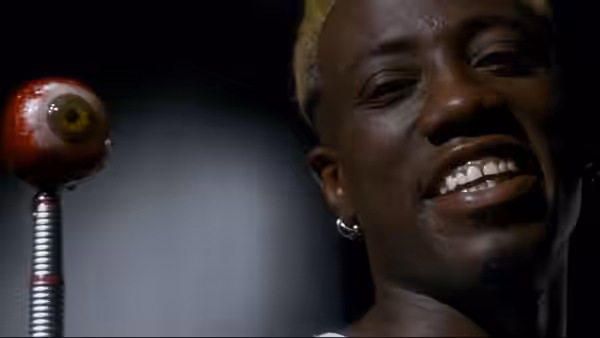 Simon Phoenix (Wesley Snipes) grins beside a robotic eye on a metal stalk