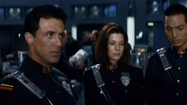 John Spartan, Lenina Huxley and a fellow officer stand in a control room