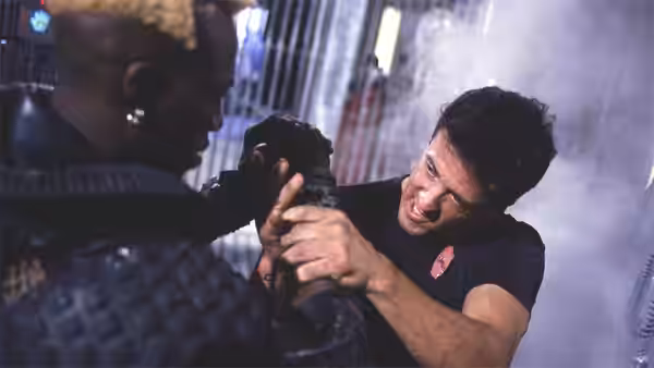 John Spartan grapples with Simon Phoenix in a smoky, industrial corridor