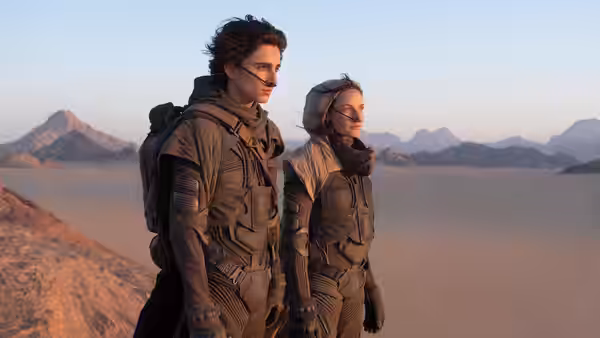 Paul Atreides (Timothée Chalamet) standing beside a woman in a desert landscape