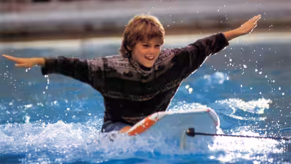 Jesse (Jason James Richter) balances on a surfboard in the water, arms spread wide