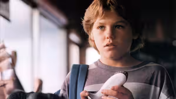 Jesse (Jason James Richter) holds a small white object indoors, looking toward someone offscreen