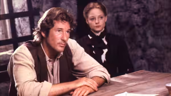 John Sommersby (Richard Gere) rests his arms on a table as Laurel watches behind him
