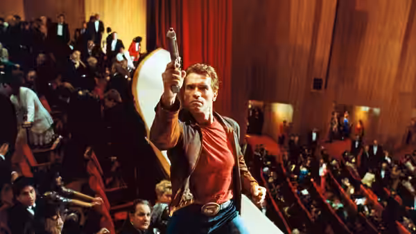 Jack Slater (Arnold Schwarzenegger) raises a gun before a seated audience in a grand hall