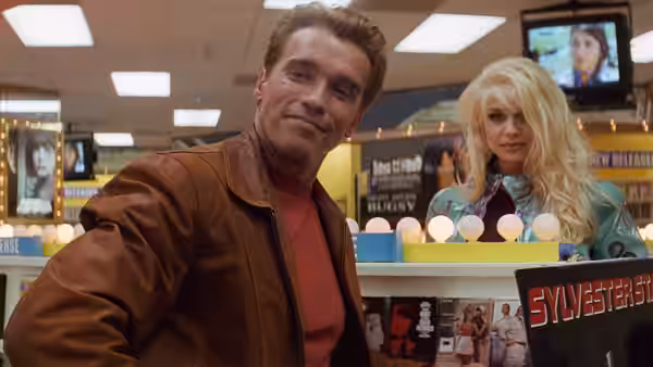 Jack Slater (Arnold Schwarzenegger) leans over a video store counter beside Whitney (Bridgette Wilson)
