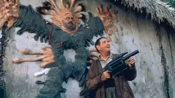 Topper Harley (Charlie Sheen) holds a machine gun beside a mounted creature in a stone corridor