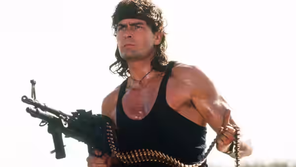 Topper Harley (Charlie Sheen) grips a machine gun and ammunition belt outdoors