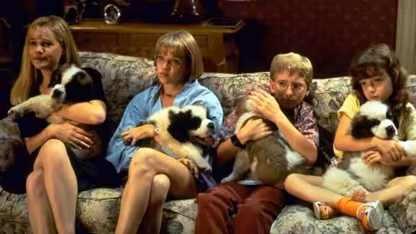 Four children sit together on a sofa, each holding a black-and-white puppy