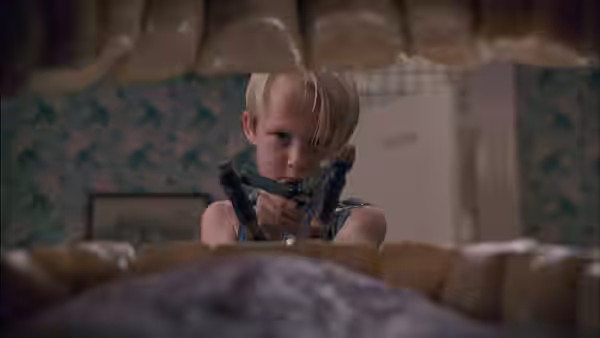 Dennis Mitchell (Mason Gamble) peers over a bed while holding a slingshot