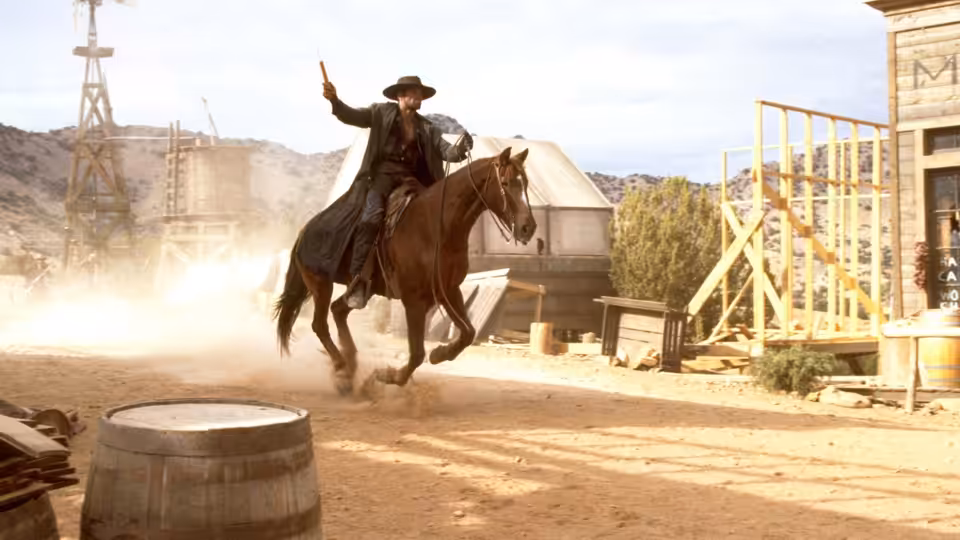 Jesse Lee (Mario Van Peebles) rides a horse through a dusty town, raising one hand