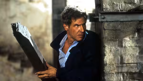 Jack Ryan (Harrison Ford) crouches beside a stone wall, gripping a jagged piece of debris