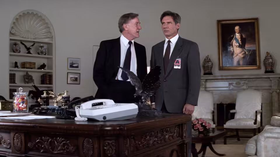 President Bennett (Donald Moffat) and Jack Ryan (Harrison Ford) stand beside a desk in the presidential office