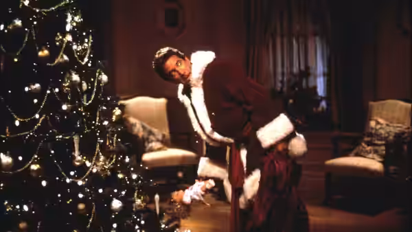 Scott Calvin (Tim Allen), dressed as Santa, bends beside a decorated Christmas tree