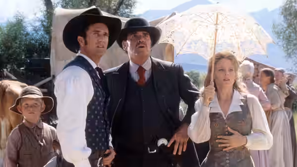 Bret Maverick (Mel Gibson) and a mustached man stand beside Annabelle Bransford (Jodie Foster), holding a parasol outdoors