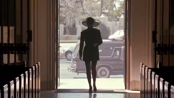 A woman in a hat enters a building as a dark car waits outside