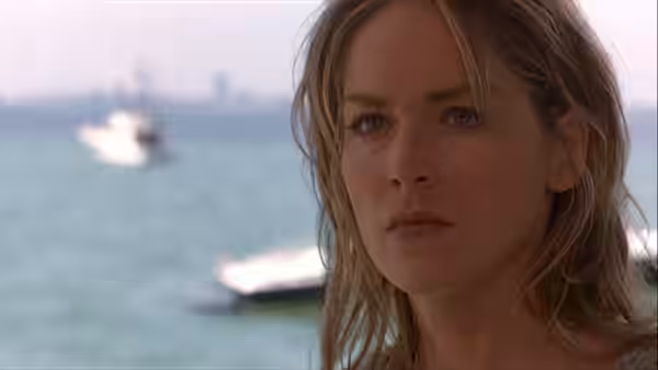 May Munro (Sharon Stone) stands by the water with boats behind her