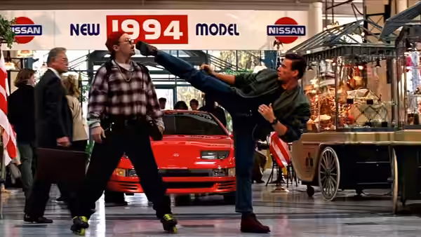 Max Walker (Jean-Claude Van Damme) kicks a man beside a red car at an auto show