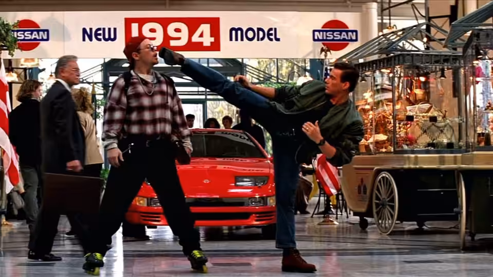 Max Walker (Jean-Claude Van Damme) kicks a man beside a red car at an auto show
