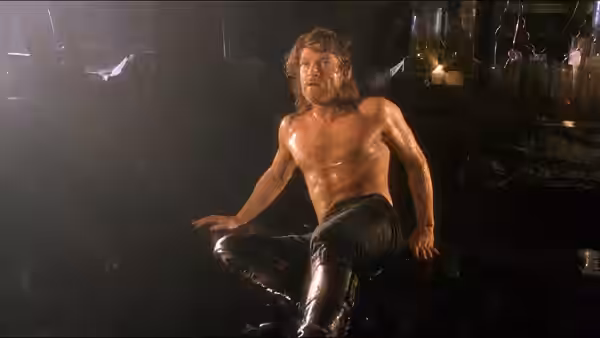 The Creature sits shirtless on the floor of a dim laboratory