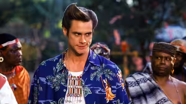 Ace Ventura (Jim Carrey) stands among villagers in a patterned shirt and ceremonial necklace