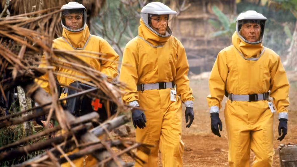 Three workers in yellow protective suits walk along a debris-strewn path