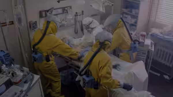 Workers in protective suits tend to a patient in a hospital room