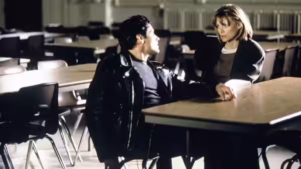 Louanne Johnson (Michelle Pfeiffer) sits with a student among desks in an empty classroom