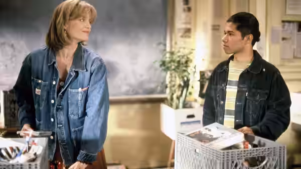 Louanne Johnson (Michelle Pfeiffer) and Raul Sanchero (Renoly Santiago) stand beside baskets of books in a classroom