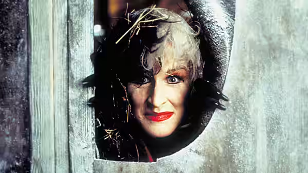 Cruella de Vil (Glenn Close) peers through a small opening in a wooden door