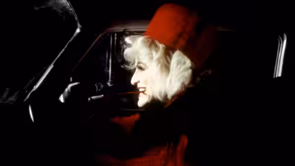 Cruella de Vil (Glenn Close) rides in a car wearing a red hat