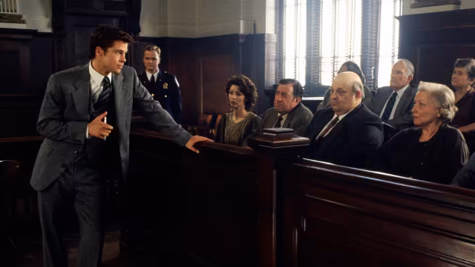 A lawyer addresses the courtroom while the defendant and spectators watch from the benches