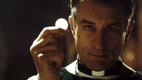 Father Bobby (Robert De Niro) raises a communion wafer